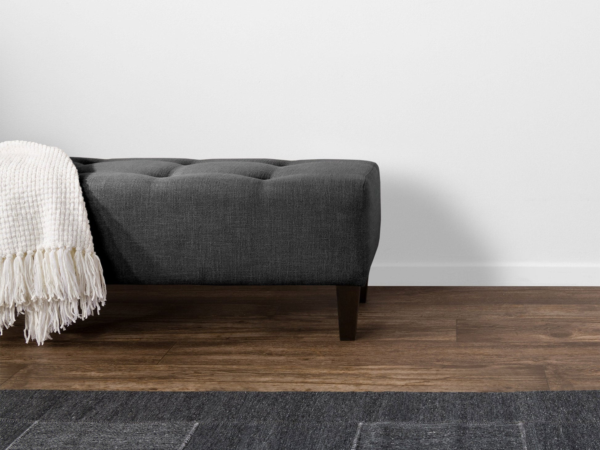 Dark grey accent bench with tufted fabric, wooden legs, and modern minimalist design.