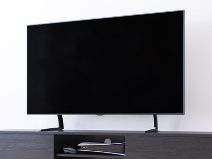 Black TV base stand with sleek design, supports TVs up to 70 inches, sturdy metal construction, minimalist style.