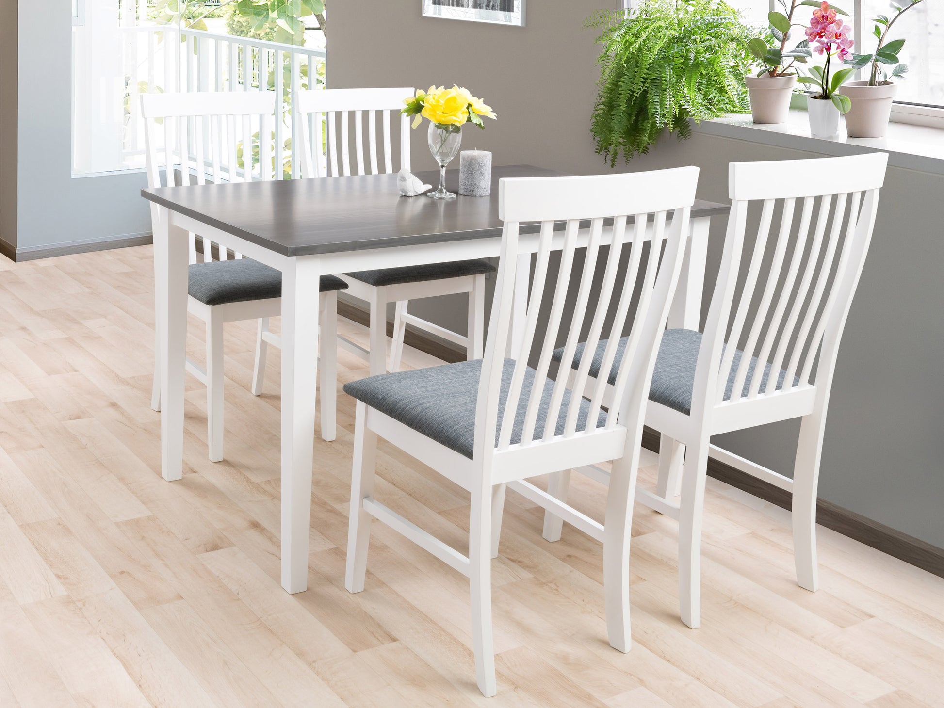 Modern dining set with a rectangular wooden table, white metal legs, and four matching chairs featuring white cushioned seats and wooden backs, set in a minimalist dining room with light wood flooring and neutral decor.