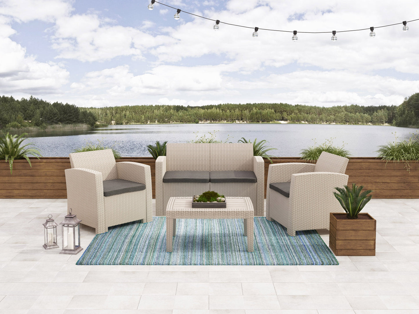 Grey wicker patio conversation set with beige cushions, featuring a glass-top coffee table, two armchairs, and a loveseat, arranged on a wooden deck with a lush green garden background.