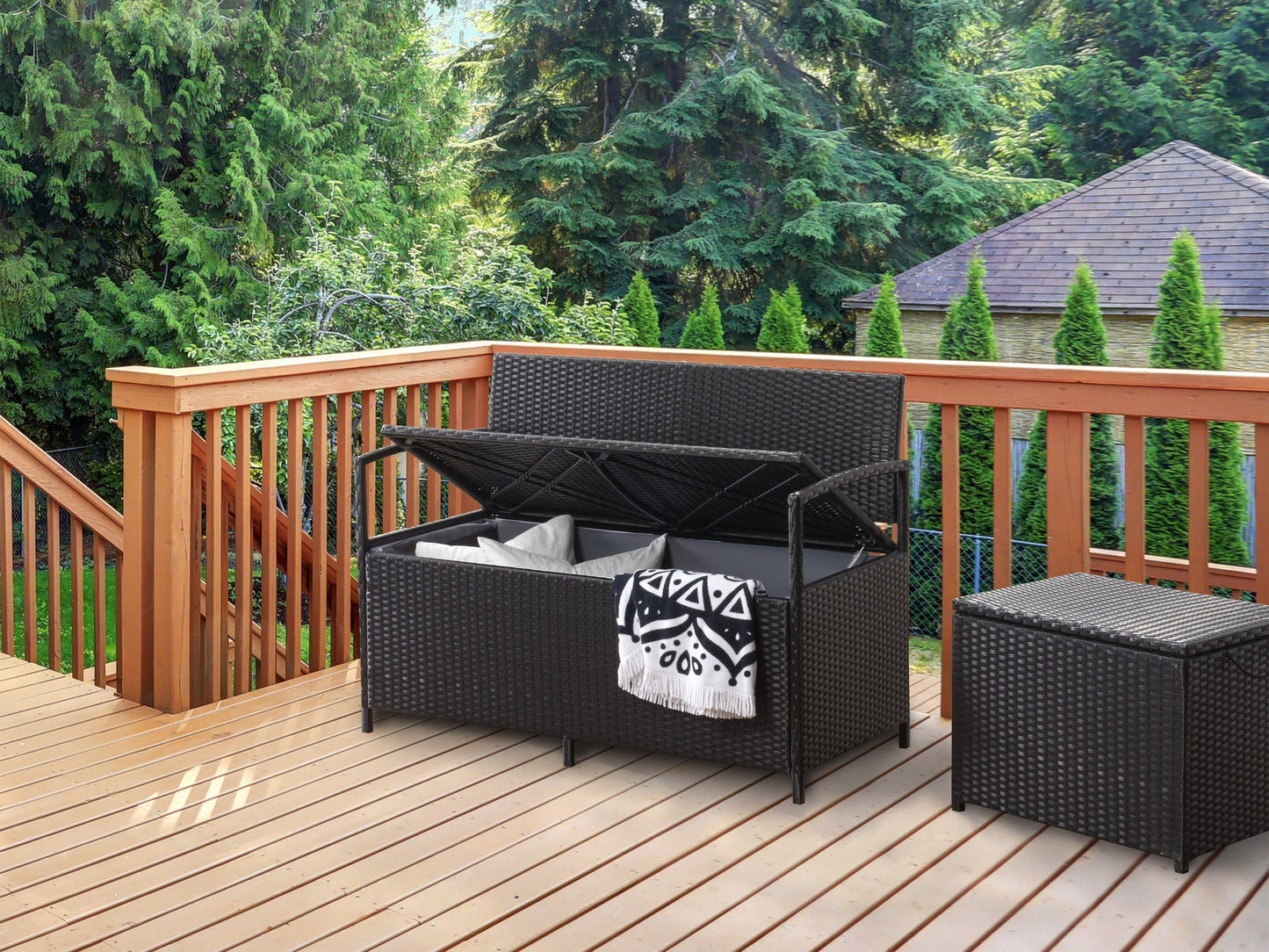 Modern patio bench with brown wooden slats, black metal frame, and armrests, placed on a concrete patio with green plants in the background. Ideal for outdoor seating and garden decor.